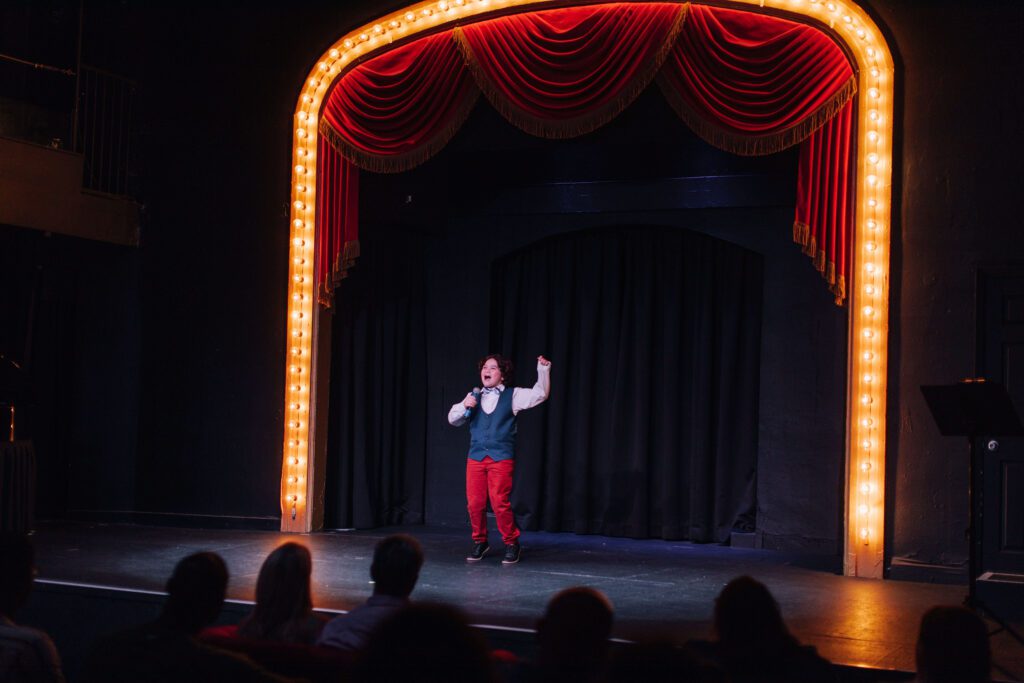 Performer on a theatre stage with marquee lights during a recital