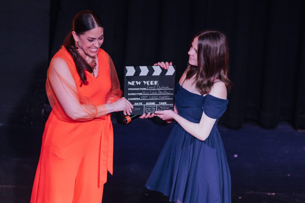 Christina Walker on stage with a performer holding a film clapperboard