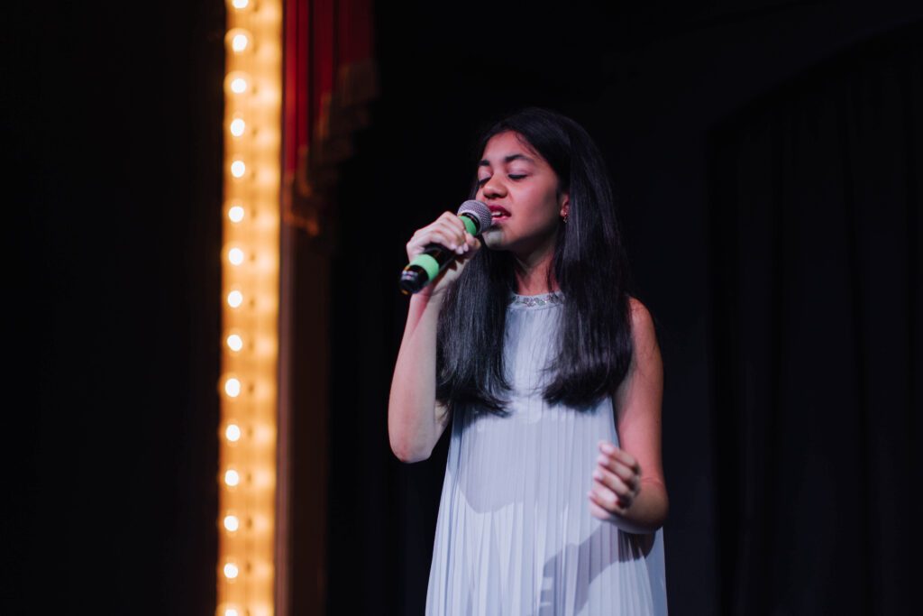 Young vocal student singing into a microphone on stage at a recital